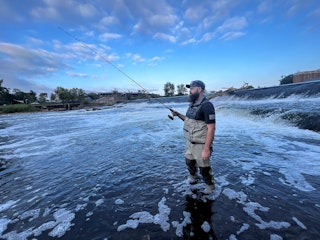 Man wades in St. Joseph river with fishing rod.