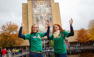 Two girls pose in front of Touchdown Jesus